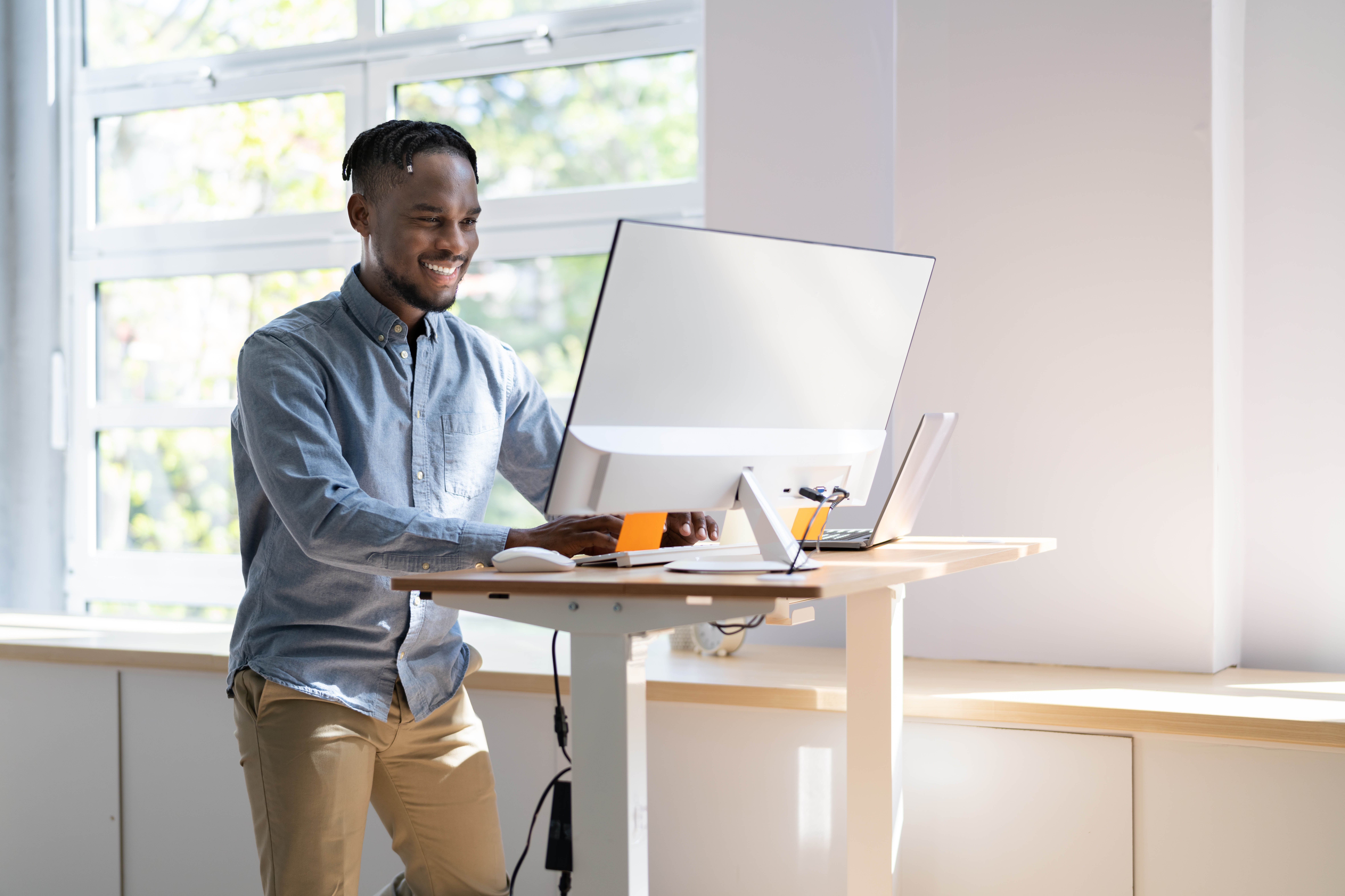 Young, professional black man stands at his standing desk completing work on the screen Young, professional black man stands at his standing desk completing work on the screen